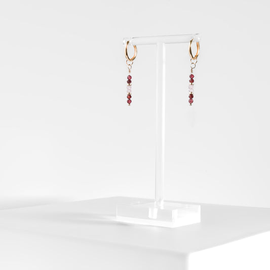 gold filled hoop earrings with garnet and pink zircon faceted bead drops on a clear acrylic earring stand