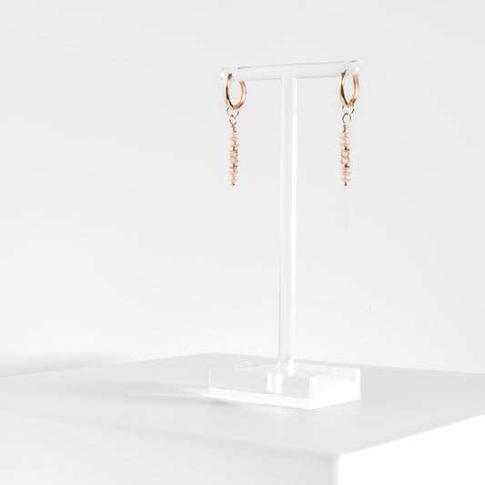 peach button pearl and peach zircon drop earrings on gold-filled huggie hoops on a clear acrylic earring stand