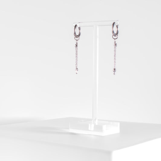 stainless steel hoop earrings with satellite chain drops on a clear acrylic earring stand
