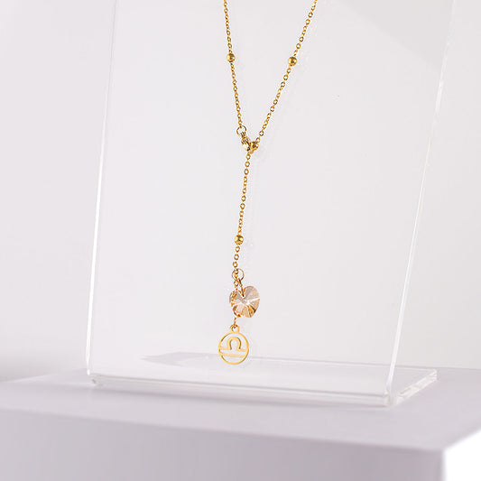 an 18K gold over stainless steel beaded station lariat necklace with a lobster claw clasp, Libra charm and golden crystal heart on a clear acrylic stand zoomed in