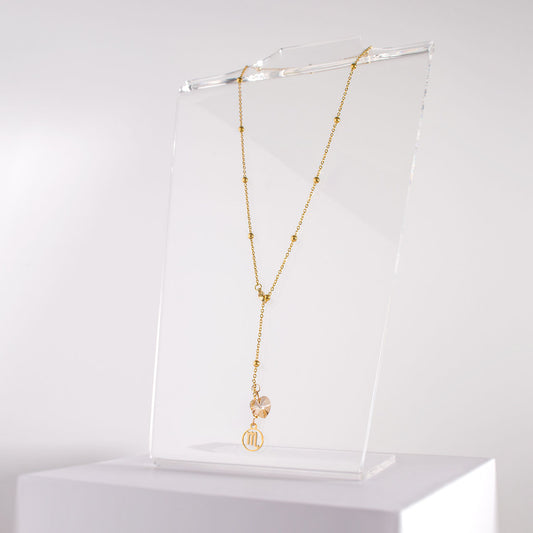 an 18K gold over stainless steel beaded station lariat necklace with a lobster claw clasp, Scorpio charm and golden crystal heart on a clear acrylic stand