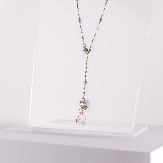 a stainless steel beaded station lariat necklace with a lobster claw clasp, Capricorn charm and black diamond crystal heart on a clear acrylic stand zoomed in